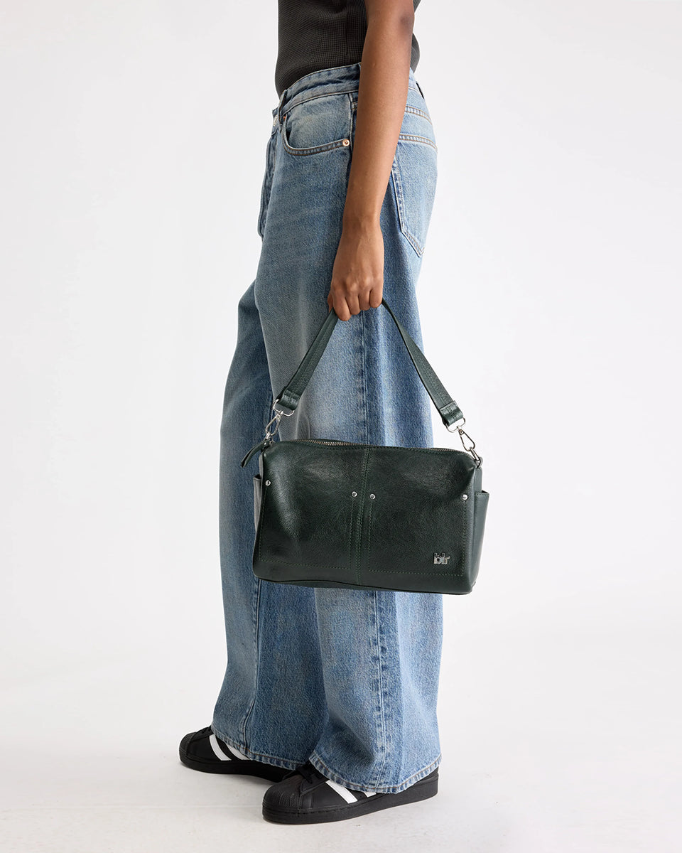 Torebka typu crossbody Duol Bottle Green marki BELLEROSE z teksturowanej, butelkowo-zielonej skóry koziej. Posiada regulowany, odpinany, beżowy pasek bawełniany oraz krótki, skórzany uchwyt. Zapinana na zamek błyskawiczny. Z przodu ma metalowe logo marki. Posiada wewnętrzną kieszeń główną, wewnętrzną kieszeń naszywaną oraz zewnętrzną kieszonkę boczną.&nbsp;