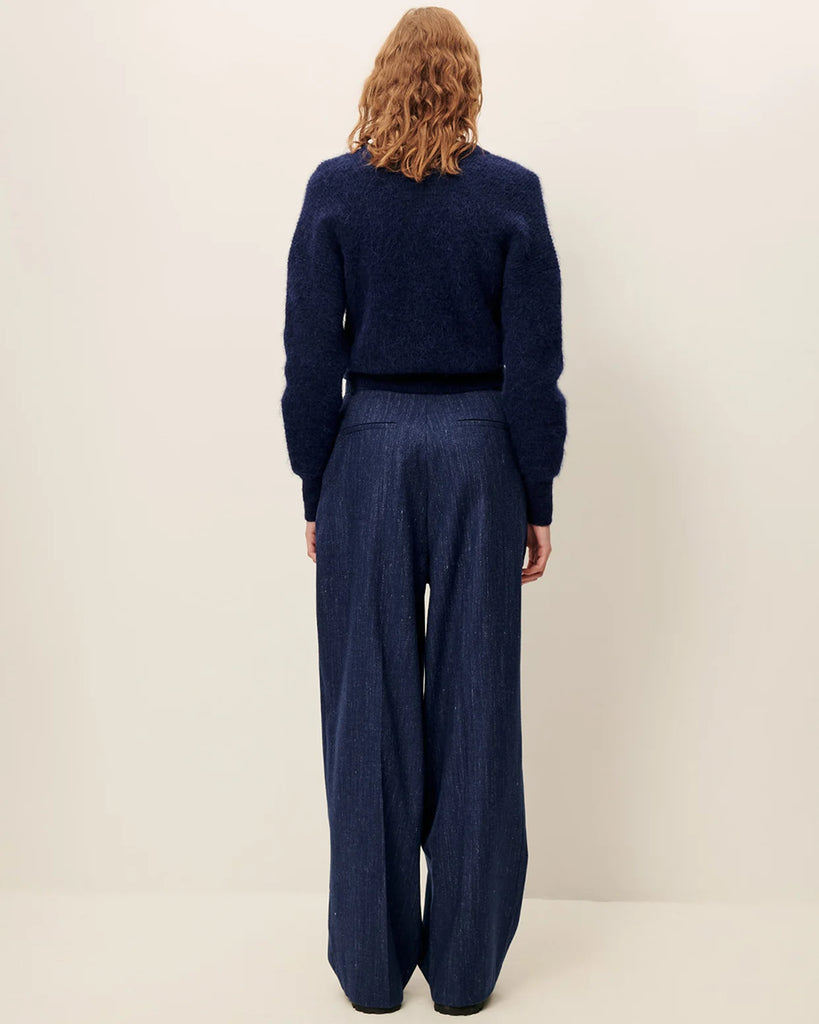 Niebieskie spodnie Emile Queen Blue francuskiej marki Sessun z wysokim stanem, z zakładkami w talii, uszyte z eleganckiej flaneli z melanżowej przędzy. &nbsp;Mają zapięcie na suwak z wewnętrznym haftem, kieszenie skośne z przodu i kieszenie z patką z tyłu. Przez całą długość nogawki widoczne są wyraźne kanty.&nbsp;