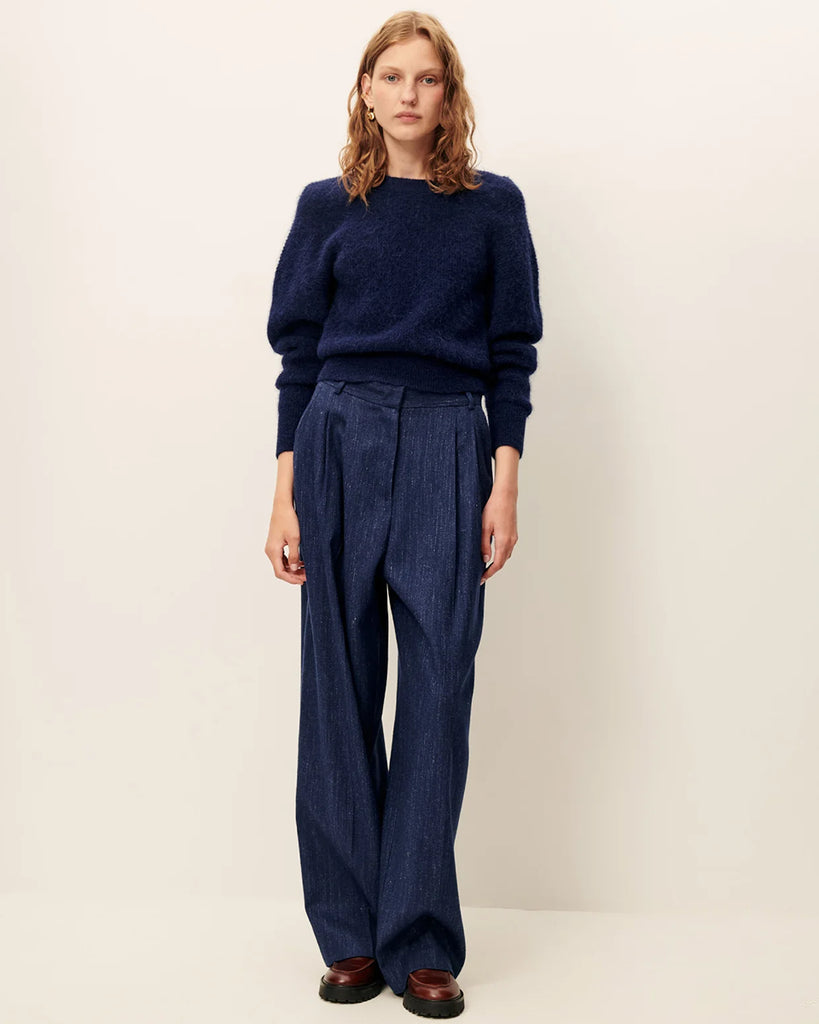 Niebieskie spodnie Emile Queen Blue francuskiej marki Sessun z wysokim stanem, z zakładkami w talii, uszyte z eleganckiej flaneli z melanżowej przędzy. &nbsp;Mają zapięcie na suwak z wewnętrznym haftem, kieszenie skośne z przodu i kieszenie z patką z tyłu. Przez całą długość nogawki widoczne są wyraźne kanty.&nbsp;