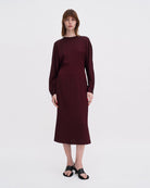 Minimalistyczna, luźna, elegancka sukienka midi Filippa K z okrągłym dekoltem i długimi rękawami rozszerzanymi pod pachami z guzikami przy mankietach. Na plecach posiada długie, wąskie rozcięcie. Z tyłu przy szyi zapinana na jeden guzik. Lekko zwężana w talii. Z tyłu w pasie ma elastyczną gumkę.