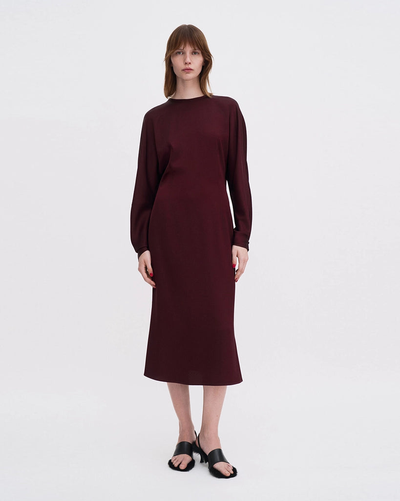 Minimalistyczna, luźna, elegancka sukienka midi Filippa K z okrągłym dekoltem i długimi rękawami rozszerzanymi pod pachami z guzikami przy mankietach. Na plecach posiada długie, wąskie rozcięcie. Z tyłu przy szyi zapinana na jeden guzik. Lekko zwężana w talii. Z tyłu w pasie ma elastyczną gumkę.