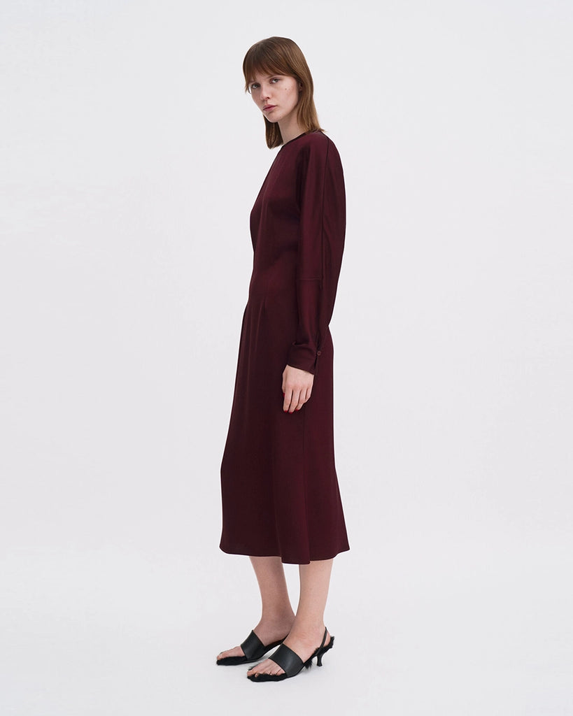 Minimalistyczna, luźna, elegancka sukienka midi Filippa K z okrągłym dekoltem i długimi rękawami rozszerzanymi pod pachami z guzikami przy mankietach. Na plecach posiada długie, wąskie rozcięcie. Z tyłu przy szyi zapinana na jeden guzik. Lekko zwężana w talii. Z tyłu w pasie ma elastyczną gumkę.