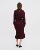 Minimalistyczna, luźna, elegancka sukienka midi Filippa K z okrągłym dekoltem i długimi rękawami rozszerzanymi pod pachami z guzikami przy mankietach. Na plecach posiada długie, wąskie rozcięcie. Z tyłu przy szyi zapinana na jeden guzik. Lekko zwężana w talii. Z tyłu w pasie ma elastyczną gumkę.