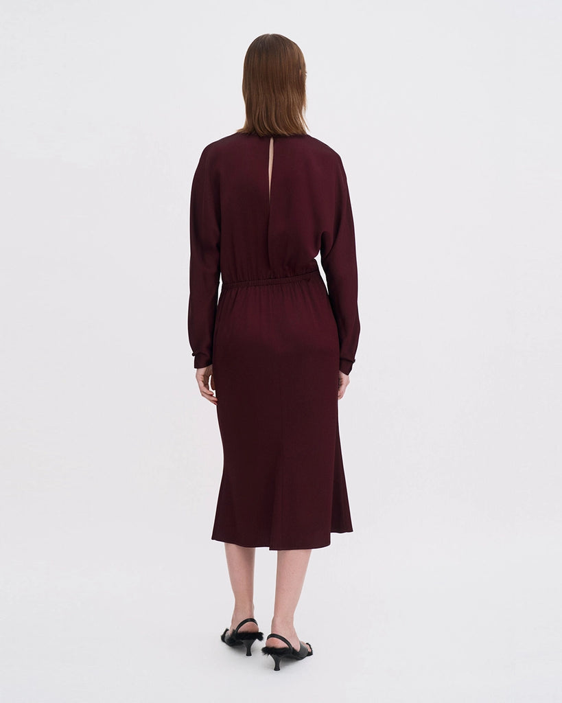 Minimalistyczna, luźna, elegancka sukienka midi Filippa K z okrągłym dekoltem i długimi rękawami rozszerzanymi pod pachami z guzikami przy mankietach. Na plecach posiada długie, wąskie rozcięcie. Z tyłu przy szyi zapinana na jeden guzik. Lekko zwężana w talii. Z tyłu w pasie ma elastyczną gumkę.