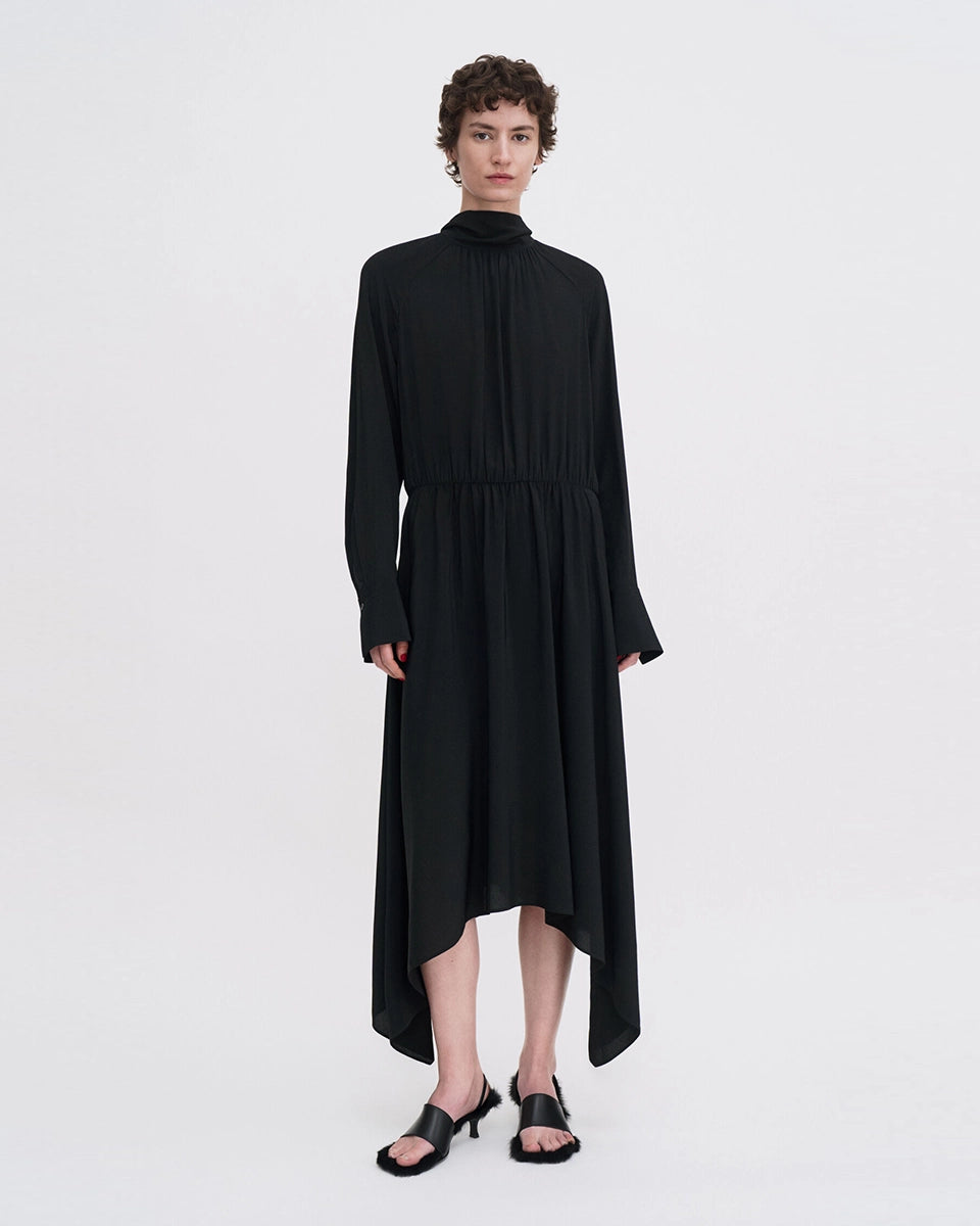 Minimalistyczna, luźna, elegancka sukienka midi Filippa K z wysokim dekoltem w formie golfu i wiązaniem z tyłu przy szyi. Sukienka ma długie rękawy zakończone mankietami oraz efektowne, wąskie rozcięcie na plecach. Z przodu marszczona przy dekolcie i i talii. U dołu wykończona asymetrycznie