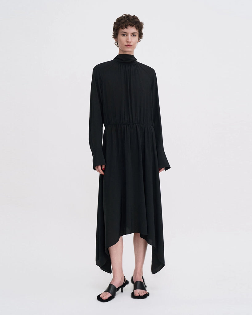 Minimalistyczna, luźna, elegancka sukienka midi Filippa K z wysokim dekoltem w formie golfu i wiązaniem z tyłu przy szyi. Sukienka ma długie rękawy zakończone mankietami oraz efektowne, wąskie rozcięcie na plecach. Z przodu marszczona przy dekolcie i i talii. U dołu wykończona asymetrycznie