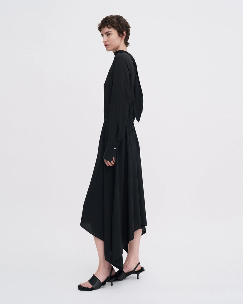 Minimalistyczna, luźna, elegancka sukienka midi Filippa K z wysokim dekoltem w formie golfu i wiązaniem z tyłu przy szyi. Sukienka ma długie rękawy zakończone mankietami oraz efektowne, wąskie rozcięcie na plecach. Z przodu marszczona przy dekolcie i i talii. U dołu wykończona asymetrycznie