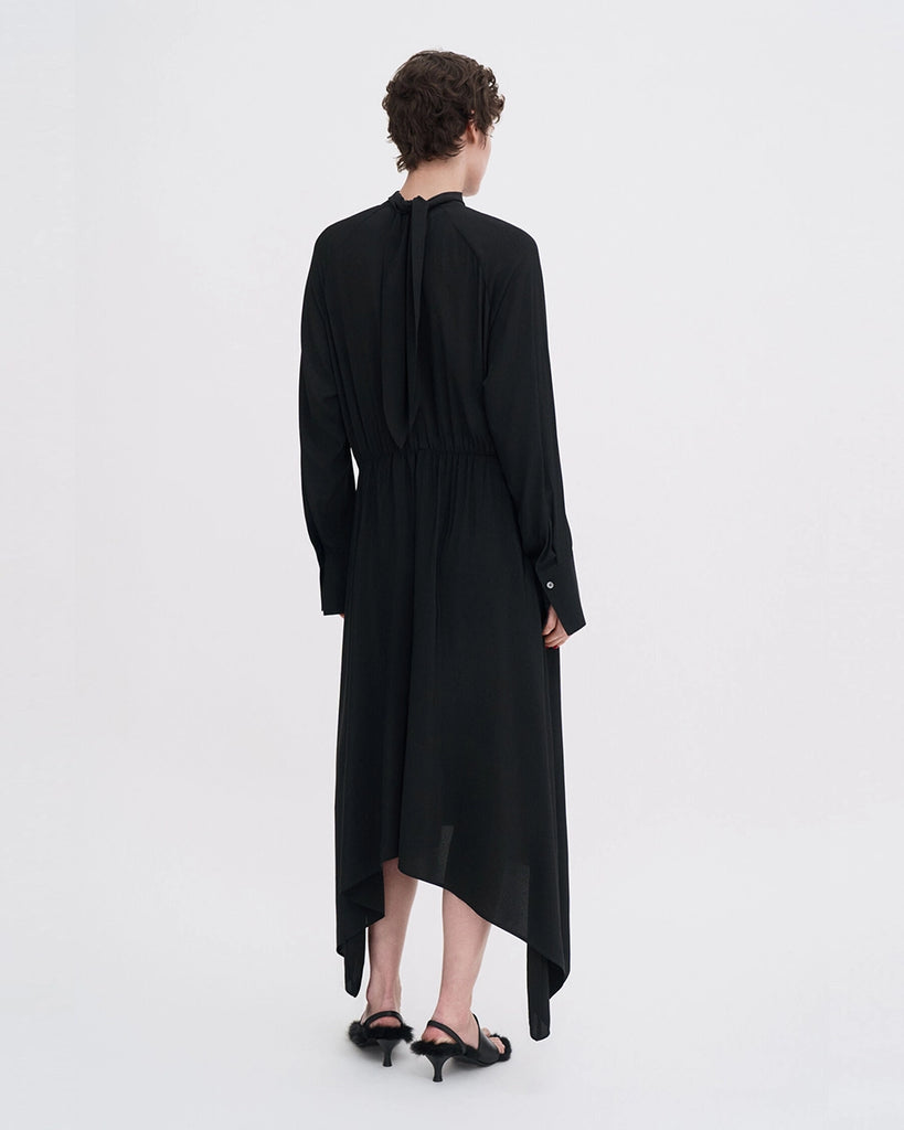 Minimalistyczna, luźna, elegancka sukienka midi Filippa K z wysokim dekoltem w formie golfu i wiązaniem z tyłu przy szyi. Sukienka ma długie rękawy zakończone mankietami oraz efektowne, wąskie rozcięcie na plecach. Z przodu marszczona przy dekolcie i i talii. U dołu wykończona asymetrycznie