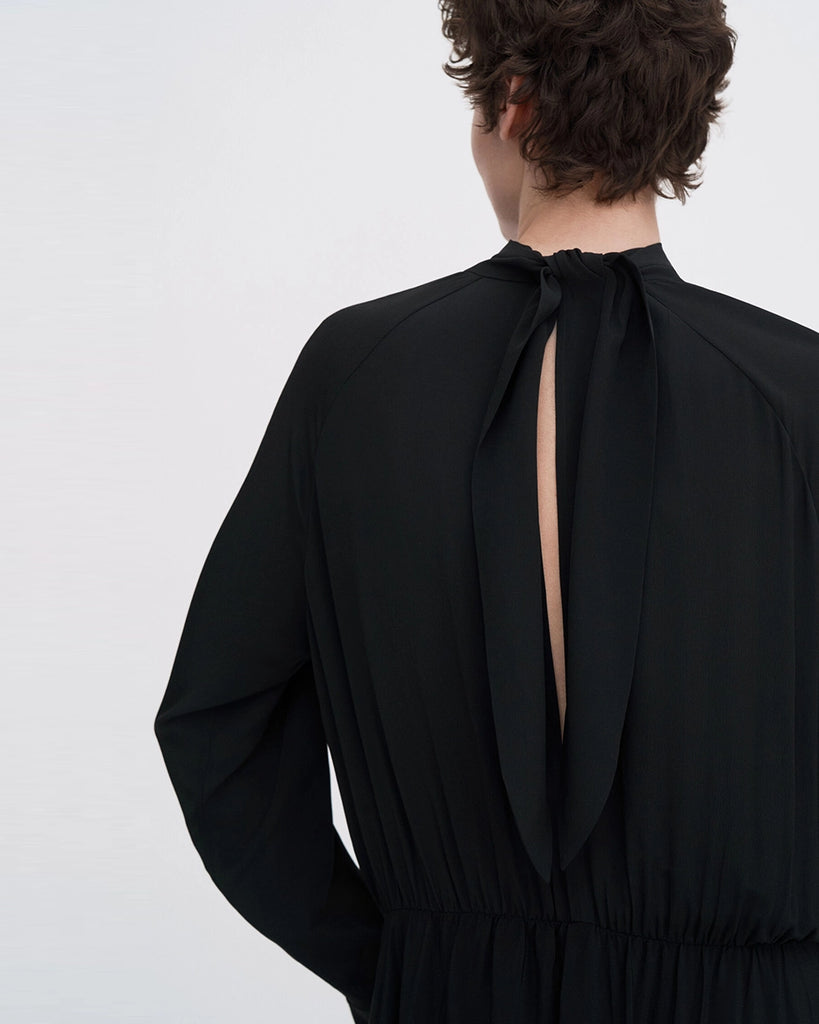 Minimalistyczna, luźna, elegancka sukienka midi Filippa K z wysokim dekoltem w formie golfu i wiązaniem z tyłu przy szyi. Sukienka ma długie rękawy zakończone mankietami oraz efektowne, wąskie rozcięcie na plecach. Z przodu marszczona przy dekolcie i i talii. U dołu wykończona asymetrycznie