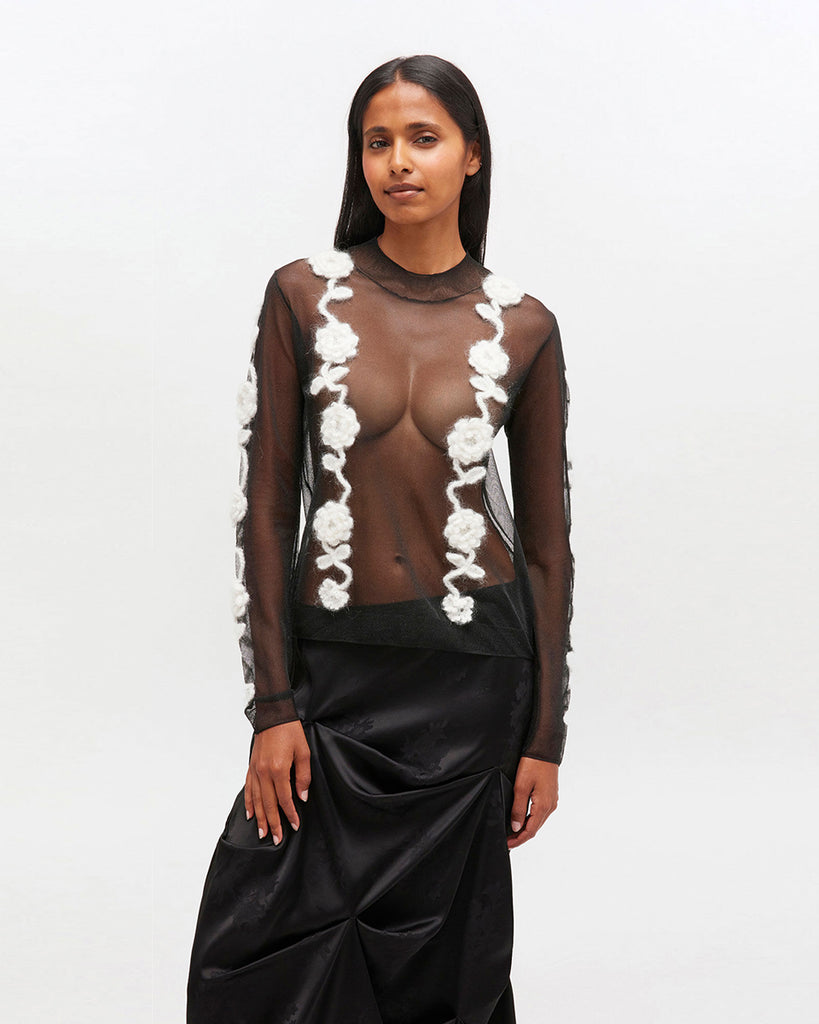 Transparentny, czarny top 2649 Ganni Black z długim rękawem i wysokim, okrągłym kołnierzykiem. Posiada zdobienia w postaci kwiatów wykonanych szydełkiem. Idealny do długiej spódnicy na eleganckie okazje.