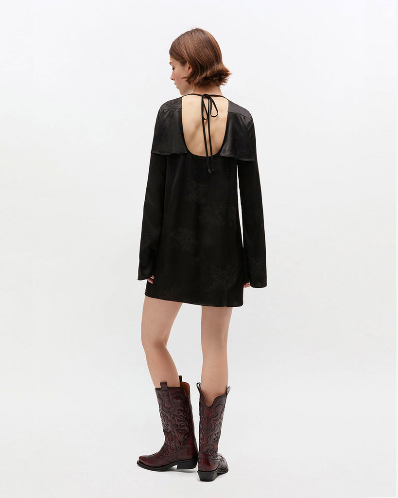 Prosta, mini sukienka 0792 GANNI Satin Black w kwiatowy print, z okrągłym dekoltem i szerokimi, długimi rękawami. Sukienka ma falbankę przy dekolcie i odkryte plecy z wiązaniem na sznurek. Wykonana z połyskliwej tkaniny.