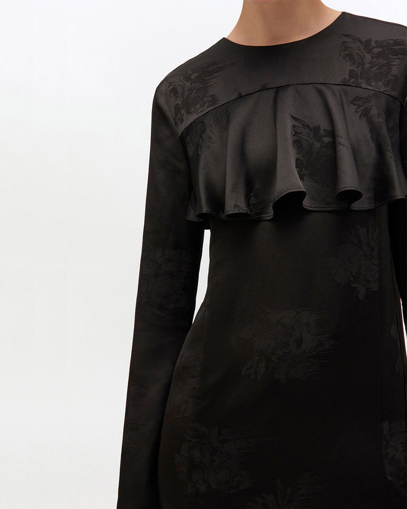 Prosta, mini sukienka 0792 GANNI Satin Black w kwiatowy print, z okrągłym dekoltem i szerokimi, długimi rękawami. Sukienka ma falbankę przy dekolcie i odkryte plecy z wiązaniem na sznurek. Wykonana z połyskliwej tkaniny.