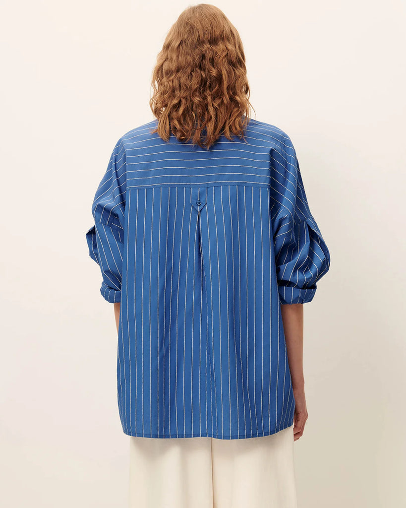 Niebieska luźna koszula Fontania Office Blue z długimi rękawami i opadającymi ramionami. Zapinana na guziki. Z przodu posiada naszywane kieszenie. Stębnowany karczek z tyłu z kontrafałdą i patką na guzik. Wykonana z kompaktowej popeliny w delikatne, teksturowane, dwukolorowe paski.&nbsp;