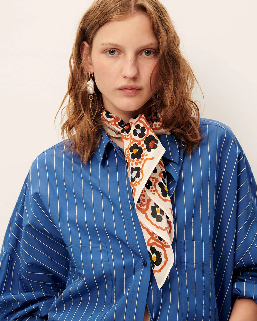 Niebieska luźna koszula Fontania Office Blue z długimi rękawami i opadającymi ramionami. Zapinana na guziki. Z przodu posiada naszywane kieszenie. Stębnowany karczek z tyłu z kontrafałdą i patką na guzik. Wykonana z kompaktowej popeliny w delikatne, teksturowane, dwukolorowe paski.&nbsp;