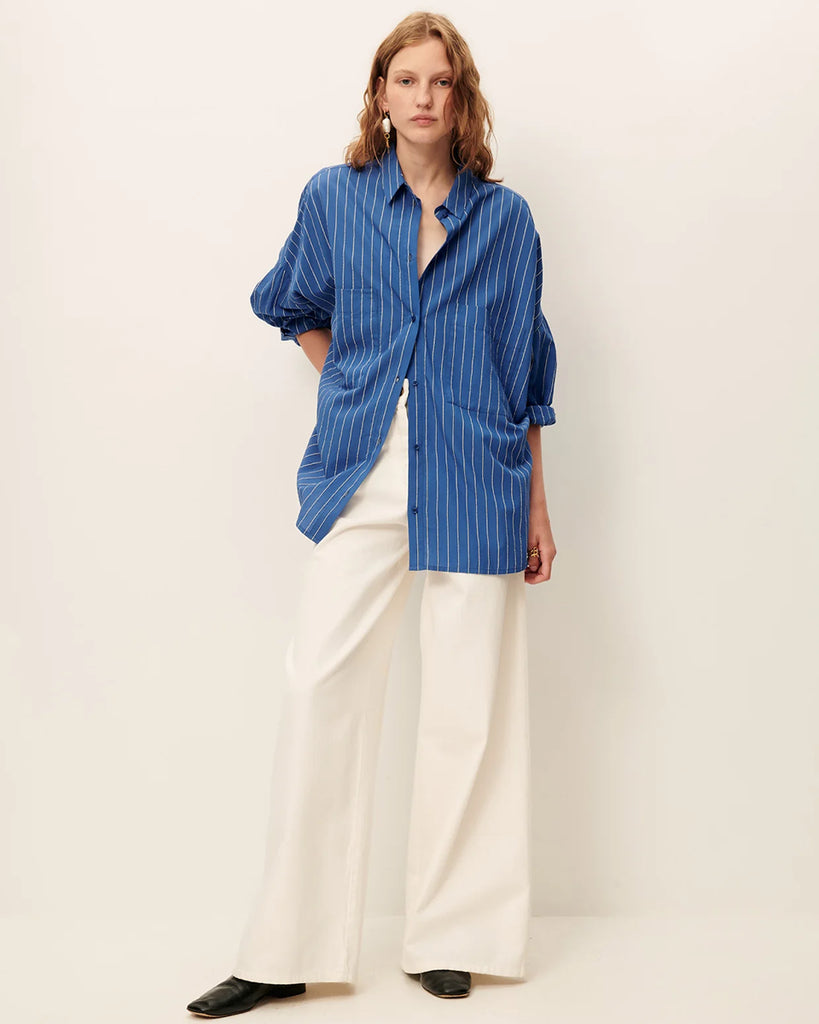 Niebieska luźna koszula Fontania Office Blue z długimi rękawami i opadającymi ramionami. Zapinana na guziki. Z przodu posiada naszywane kieszenie. Stębnowany karczek z tyłu z kontrafałdą i patką na guzik. Wykonana z kompaktowej popeliny w delikatne, teksturowane, dwukolorowe paski.&nbsp;