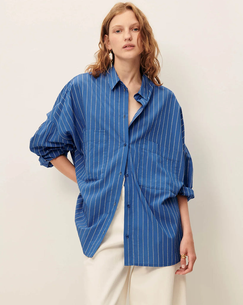 Niebieska luźna koszula Fontania Office Blue z długimi rękawami i opadającymi ramionami. Zapinana na guziki. Z przodu posiada naszywane kieszenie. Stębnowany karczek z tyłu z kontrafałdą i patką na guzik. Wykonana z kompaktowej popeliny w delikatne, teksturowane, dwukolorowe paski.&nbsp;