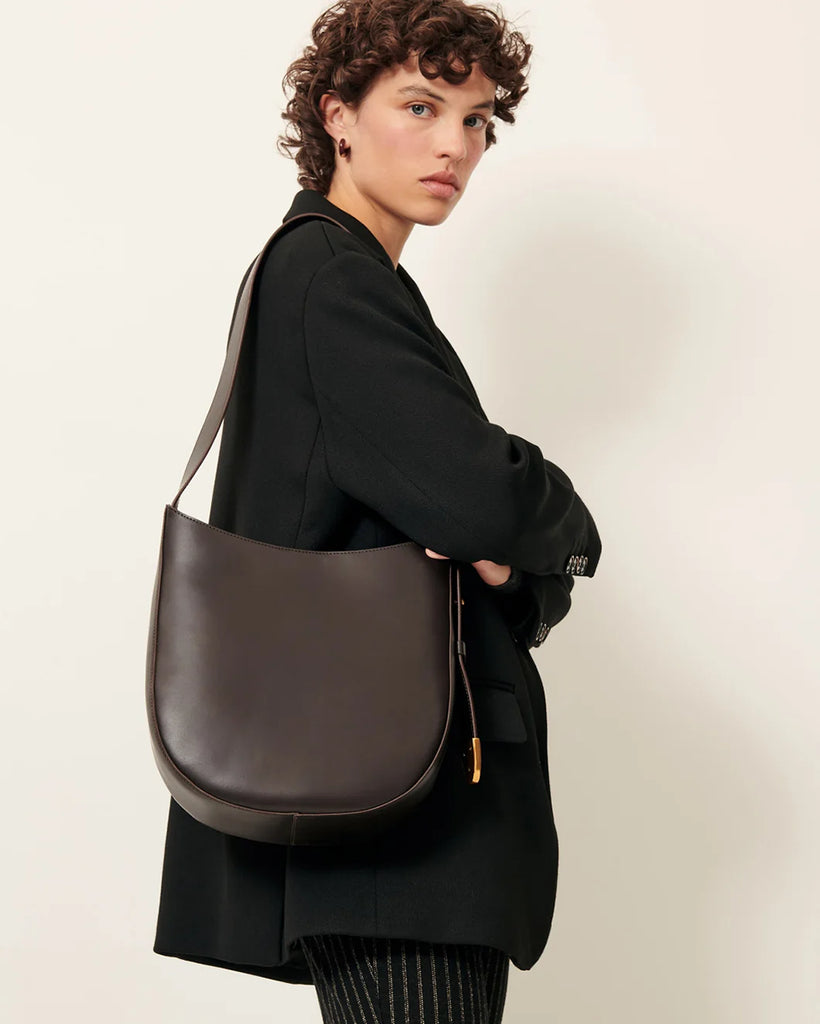 Brązowa, skórzana torba Grandę Amo Deep Coffea francuskiej marki Sessun z regulowanym paskiem na ramię. Pasek ma metalowe zakończenie z grawerunkiem marki. Torba ma jedną, centralną komorę z wewnętrzną kieszenią zapinaną na zamek. Zapinana na zatrzask.&nbsp;