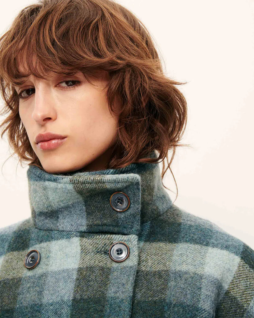 Krótki, elastyczny płaszcz Harlow Smocky Blue z miękkiej, puszystej wełny o podwójnym splocie w kratę, tkanej we Włoszech. Ma wysoki kołnierz z zapięciem na guzik, kieszenie z patką oraz ściągacz na dole i przy mankietach. Zapięcie dwurzędowe.&nbsp;