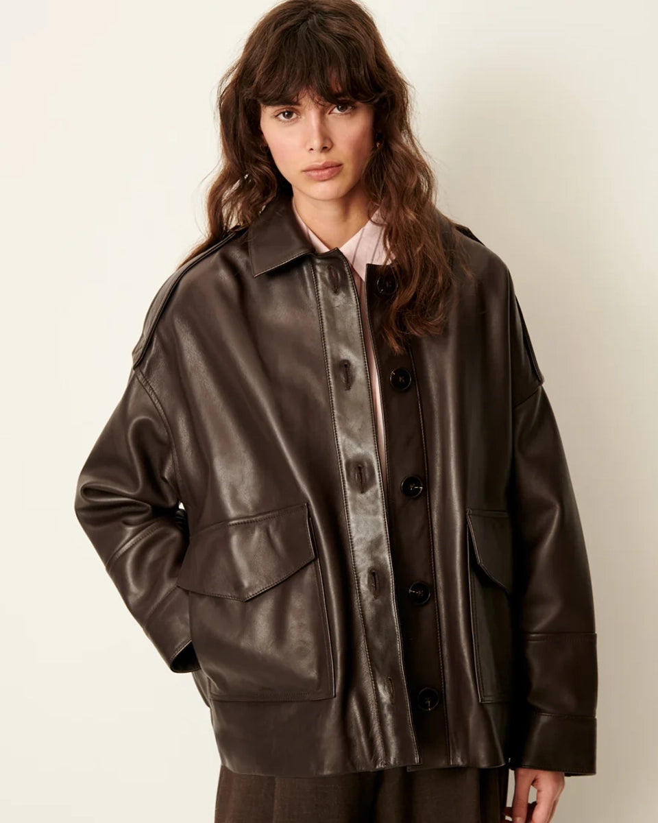 Brązowa, luźna kurtka Harriboyd Coffee Leather francuskiej marki Sessun w stylu klasycznej pilotki. Wykonana jest z gładkiej, ciemnobrązowej skóry o lekkim połysku. Z przodu zapinana jest na duże, czarne guziki, a po bokach ma duże naszywane kieszenie. Rękawy są długie, z mankietami zapinanymi na guzik