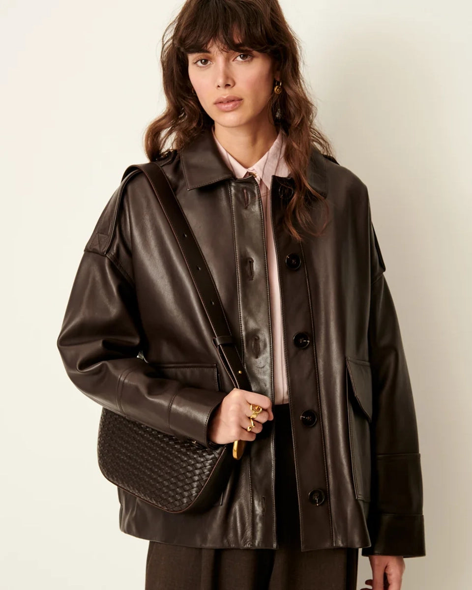Brązowa, luźna kurtka Harriboyd Coffee Leather francuskiej marki Sessun w stylu klasycznej pilotki. Wykonana jest z gładkiej, ciemnobrązowej skóry o lekkim połysku. Z przodu zapinana jest na duże, czarne guziki, a po bokach ma duże naszywane kieszenie. Rękawy są długie, z mankietami zapinanymi na guzik