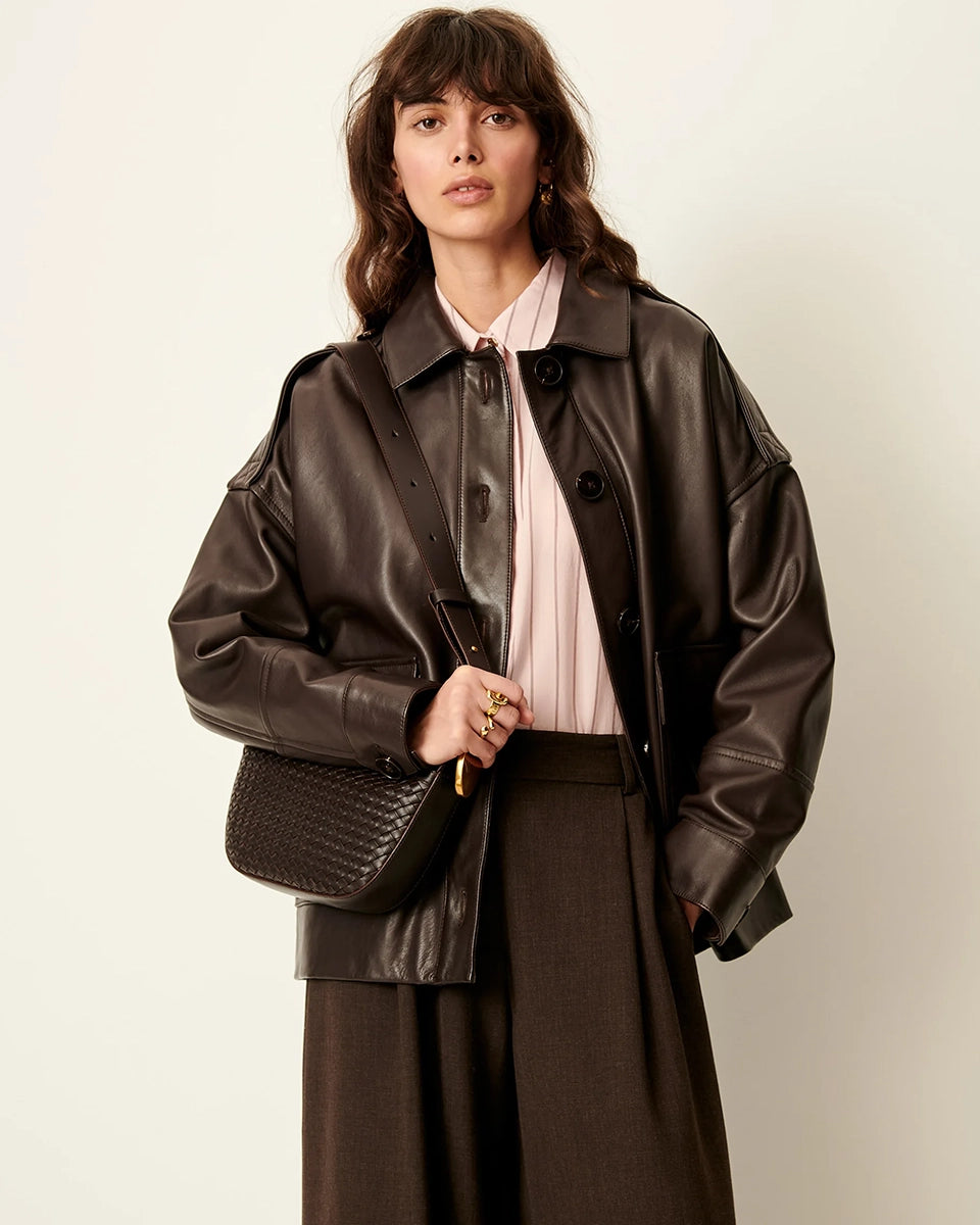 Brązowa, luźna kurtka Harriboyd Coffee Leather francuskiej marki Sessun w stylu klasycznej pilotki. Wykonana jest z gładkiej, ciemnobrązowej skóry o lekkim połysku. Z przodu zapinana jest na duże, czarne guziki, a po bokach ma duże naszywane kieszenie. Rękawy są długie, z mankietami zapinanymi na guzik