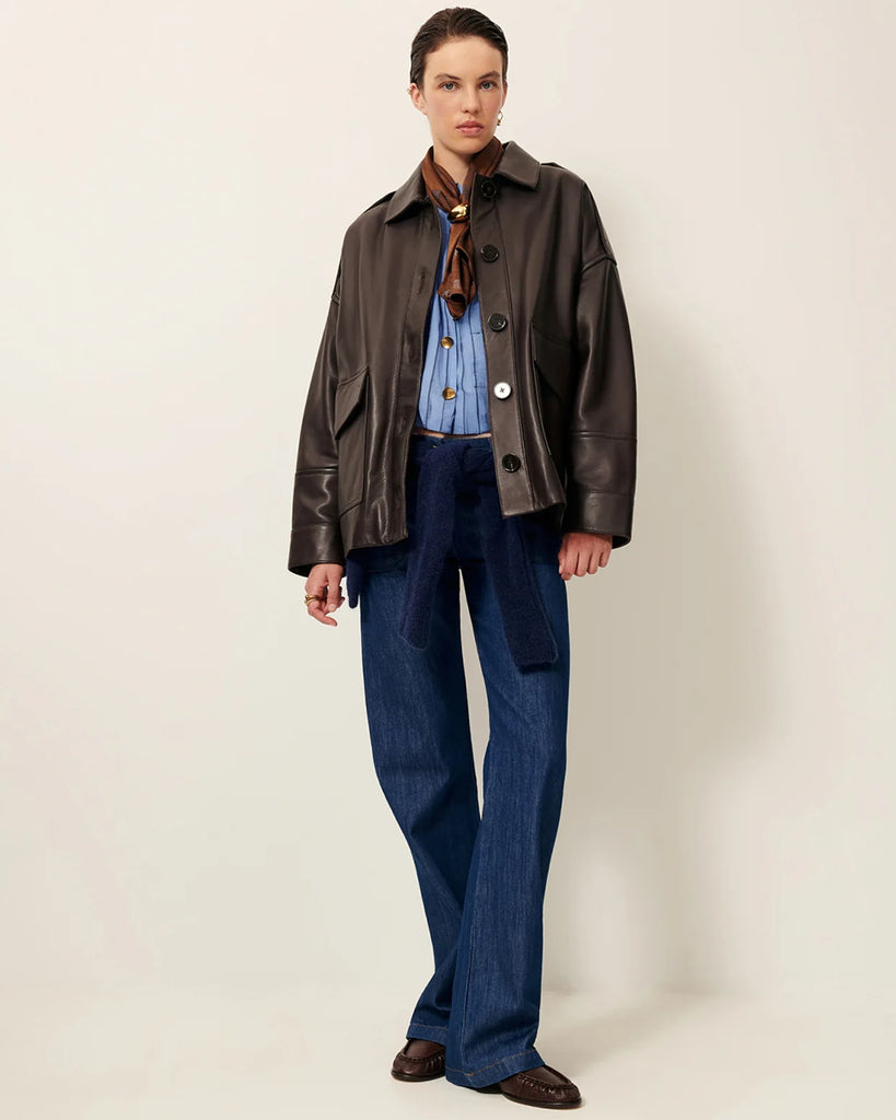 Brązowa, luźna kurtka Harriboyd Coffee Leather francuskiej marki Sessun w stylu klasycznej pilotki. Wykonana jest z gładkiej, ciemnobrązowej skóry o lekkim połysku. Z przodu zapinana jest na duże, czarne guziki, a po bogach ma duże naszywane kieszenie. Rękawy są długie, z mankietami zapinanymi na guzik. Tył kurtki jest prosty, z poziomym szwem przez plecy i elastycznym ściągaczem w dolnej części.&nbsp;