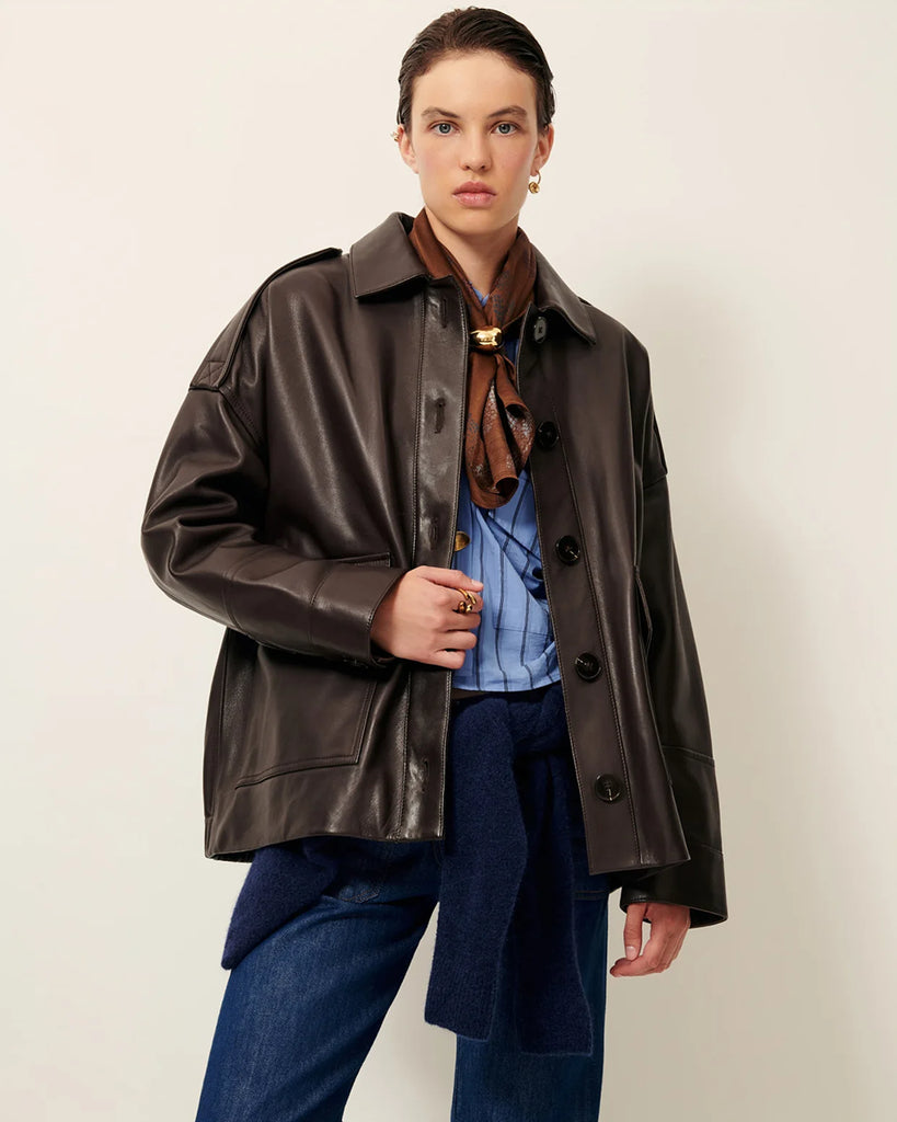 Brązowa, luźna kurtka Harriboyd Coffee Leather francuskiej marki Sessun w stylu klasycznej pilotki. Wykonana jest z gładkiej, ciemnobrązowej skóry o lekkim połysku. Z przodu zapinana jest na duże, czarne guziki, a po bogach ma duże naszywane kieszenie. Rękawy są długie, z mankietami zapinanymi na guzik. Tył kurtki jest prosty, z poziomym szwem przez plecy i elastycznym ściągaczem w dolnej części.&nbsp;