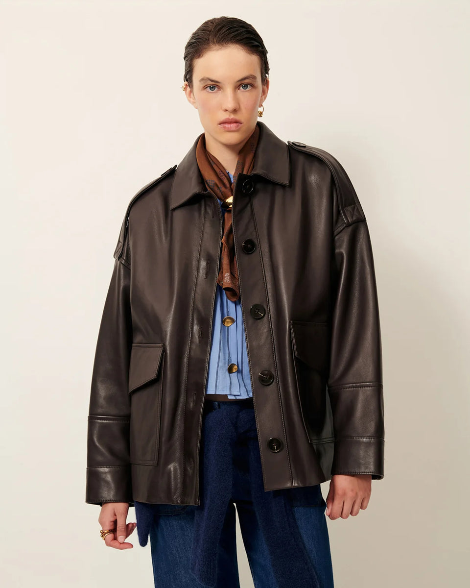 Brązowa, luźna kurtka Harriboyd Coffee Leather francuskiej marki Sessun w stylu klasycznej pilotki. Wykonana jest z gładkiej, ciemnobrązowej skóry o lekkim połysku. Z przodu zapinana jest na duże, czarne guziki, a po bogach ma duże naszywane kieszenie. Rękawy są długie, z mankietami zapinanymi na guzik. Tył kurtki jest prosty, z poziomym szwem przez plecy i elastycznym ściągaczem w dolnej części.&nbsp;