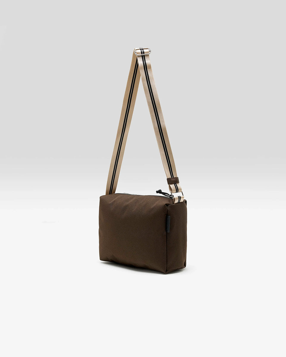 Zapinana na suwak torebka typu cross body Hobbes Dark Roast marki Bellerose z brązowego, matowego nylonu o fakturowanej powierzchni. Wyróżnia się prostokątnym kształtem, miękką konstrukcją oraz regulowanym paskiem w paski i silikonowym logo.&nbsp;