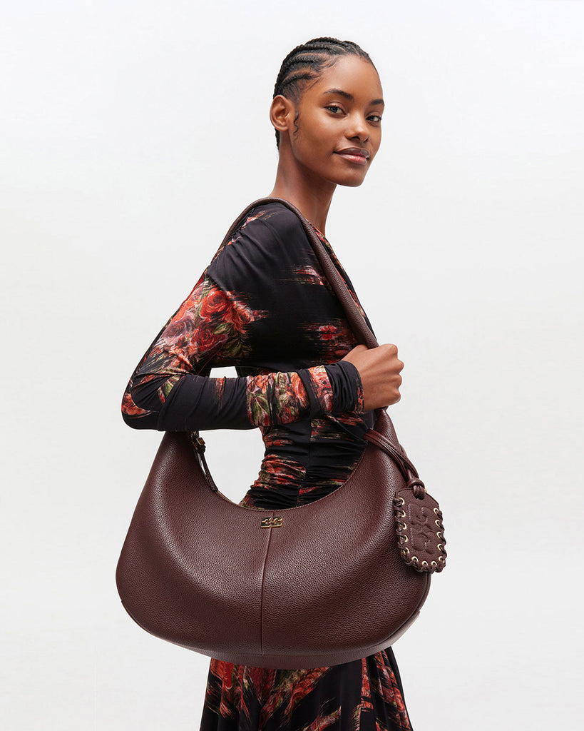 Duża, brązowa torba o kształcie półksiężyca 7298 Hobo Medium GANNI z dużą, szeroką rączką do wygodnego zawieszenia na ramieniu. Z przodu posiada niewielki wypukły logotyp marki. Z tyłu, u dołu znajduje się wytłaczany napis GANNI. Do torby dołączona jest duża, lustrzana zawieszka. Jest zapinana za pomocą zamka błyskawicznego. Wewnątrz posiada niewielką kieszonkę na najważniejsze drobiazgi takie jak klucze czy karta kredytowa. Wykonana z opatentowanego przez markę, ekologicznego materiału bedącego połączeniem