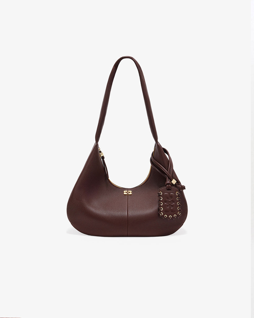 Duża, brązowa torba o kształcie półksiężyca 7298 Hobo Medium GANNI z dużą, szeroką rączką do wygodnego zawieszenia na ramieniu. Z przodu posiada niewielki wypukły logotyp marki. Z tyłu, u dołu znajduje się wytłaczany napis GANNI. Do torby dołączona jest duża, lustrzana zawieszka. Jest zapinana za pomocą zamka błyskawicznego. Wewnątrz posiada niewielką kieszonkę na najważniejsze drobiazgi takie jak klucze czy karta kredytowa. Wykonana z opatentowanego przez markę, ekologicznego materiału bedącego połączeniem