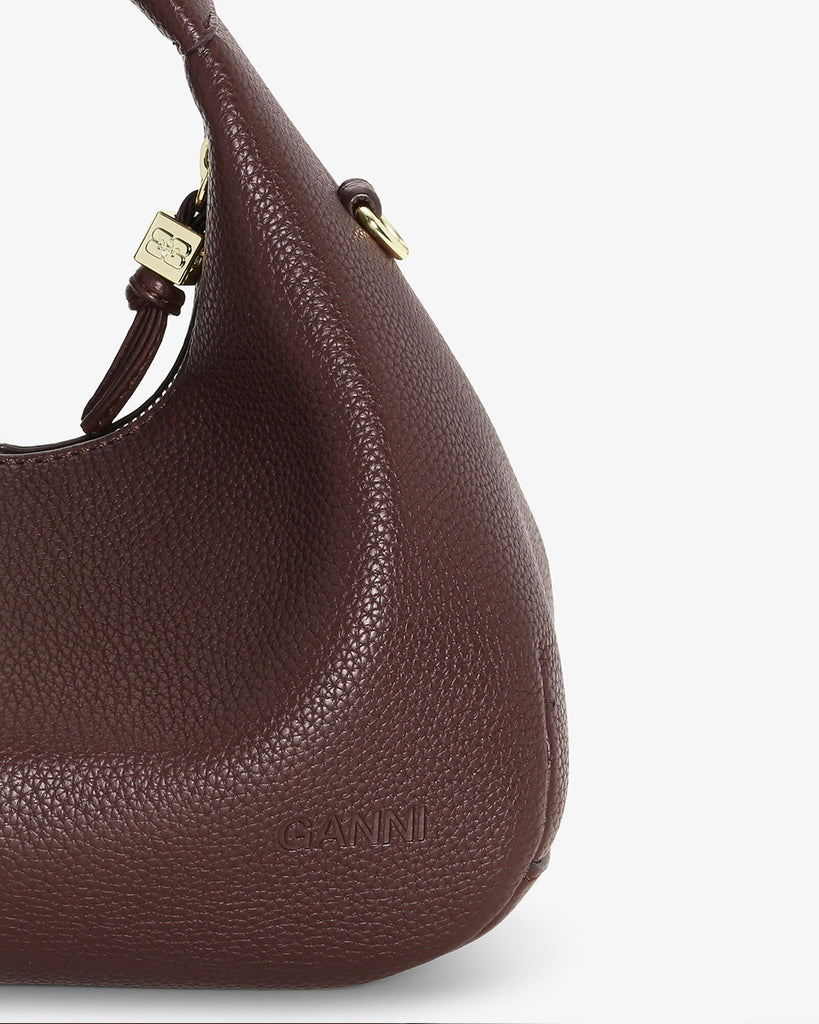 Mała, brązowa torebka w kształcie półksiężyca Hobo Mini Chicory Coffee z uchwytem i regulowanym, odpinanym paskiem oraz zapięciem na suwak. Z przodu posiada niewielki wypukły logotyp marki. Z tyłu, u dołu znajduje się wytłaczany napis GANNI. Do torebki dołączona jest lustrzana zawieszka. Wewnątrz posiada niewielką kieszonkę na najważniejsze drobiazgi takie jak klucze czy karta kredytowa.