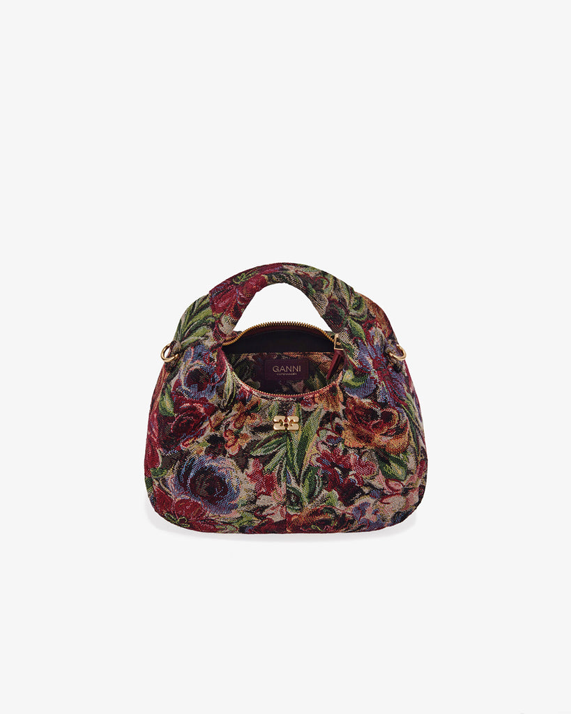 Mała torebka w kształcie półksiężyca Hobo Mini Tawny Port w kwiatowy print z uchwytem i regulowanym, odpinanym paskiem oraz zapięciem na suwak. Z przodu posiada niewielki wypukły logotyp marki. Z tyłu, u dołu znajduje się wytłaczany napis GANNI. Do torebki dołączona jest lustrzana zawieszka. Wewnątrz posiada niewielką kieszonkę na najważniejsze drobiazgi takie jak klucze czy karta kredytowa.&nbsp;