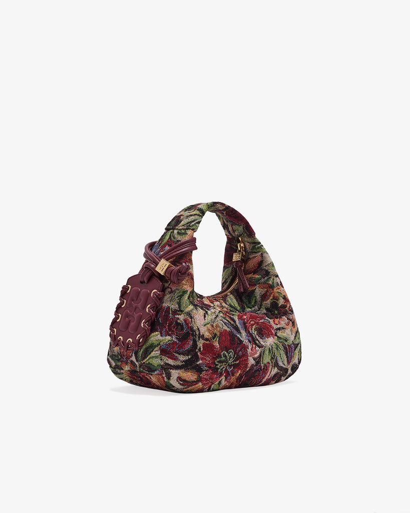 Mała torebka w kształcie półksiężyca Hobo Mini Tawny Port w kwiatowy print z uchwytem i regulowanym, odpinanym paskiem oraz zapięciem na suwak. Z przodu posiada niewielki wypukły logotyp marki. Z tyłu, u dołu znajduje się wytłaczany napis GANNI. Do torebki dołączona jest lustrzana zawieszka. Wewnątrz posiada niewielką kieszonkę na najważniejsze drobiazgi takie jak klucze czy karta kredytowa.&nbsp;