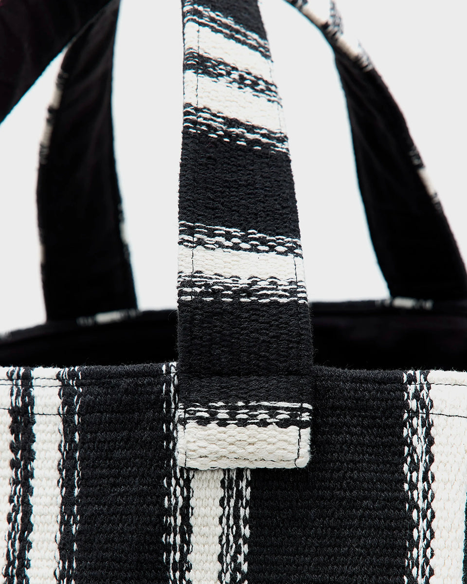 Gruba, tkana, bawełniana torba Ibox Stripe A marki Bellerose w czarno-białe paski. Bardzo pojemna w środku. Posiada solidne uchwyty, wewnętrzną kieszeń główną oraz mniejszą kieszeń z metką na imię. Na bocznym szwie widoczna jest niewielka etykieta z logo marki. Wykonana z grubej bawełny.&nbsp;