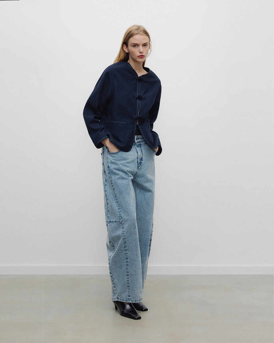 Elegancka, ciemnogranatowa, krótka kurtka Indie Black Iris o fasonie inspirowanym stylem wschodnim. Model ma prosty krój z okrągłym dekoltem bez kołnierzyka oraz długie rękawy o swobodnej linii. Charakterystycznym elementem są ozdobne, tekstylne zapięcia typu chińskiego, zwane węzełkami, które biegną wzdłuż przedniej plisy. Kurtka posiada również dwie duże, naszywane kieszenie oraz zaokrąglone doły po bokach, co nadaje jej miękki, nowoczesny wygląd. Wykonana z mieszanki z wełną.

-Inspirowana stylem wschodn