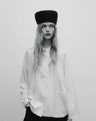 Elegancki, minimalistyczny kapelusz typu pillbox Indie TNS Black Iris wykonany z gładkiego, ciemnogranatowego filcu wełnianego. Jego konstrukcja wyróżnia się opływowym, zaokrąglonym kształtem, co nadaje mu nowoczesnego, a jednocześnie nawiązującego do stylu retro wyglądu. Kapelusz ściśle przylega do głowy, tworząc czystą, geometryczną linię, która subtelnie eksponuje rysy twarzy.&nbsp;