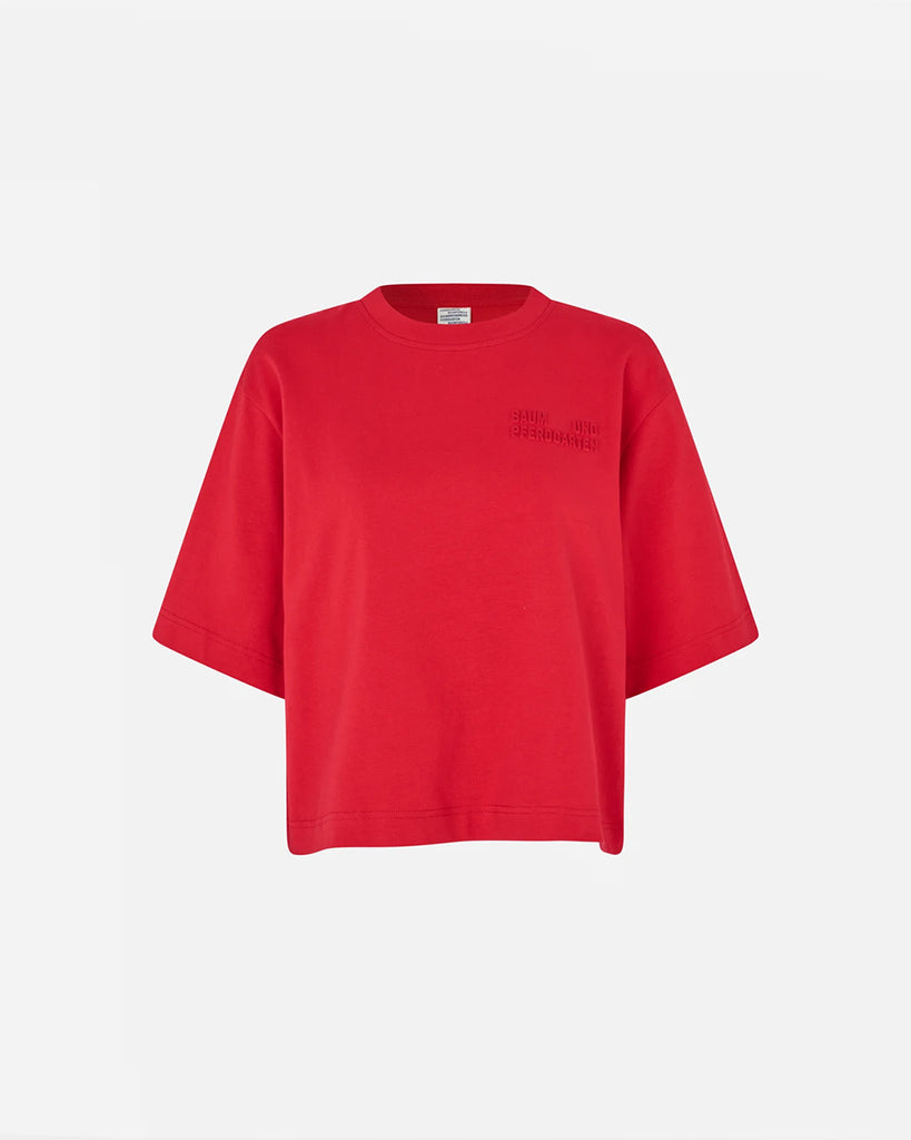 Luźny t-shirt Jiana Crimson Red w kolorze czerwonym z okrągłym dekoltem i obniżonymi ramionami. Na prawej piersi wytłoczone jest logo marki. Wykonany z miękkiej, grubej bawełny organicznej. Idealnie pasuje do klasycznych jeansów lub spodni.