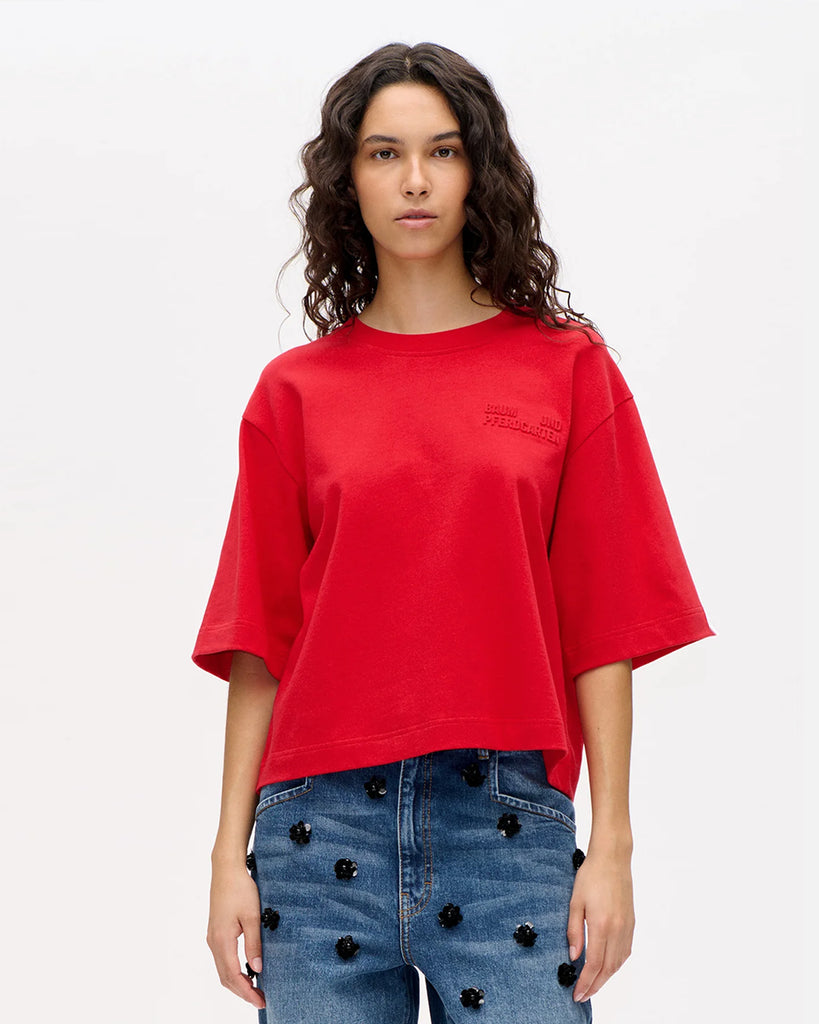 Luźny t-shirt Jiana Crimson Red w kolorze czerwonym z okrągłym dekoltem i obniżonymi ramionami. Na prawej piersi wytłoczone jest logo marki. Wykonany z miękkiej, grubej bawełny organicznej. Idealnie pasuje do klasycznych jeansów lub spodni.