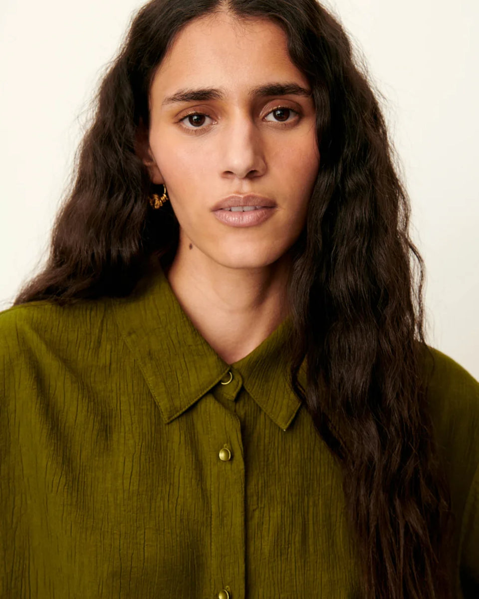 Luźna, krótka koszula Kayla Agave Green marki Sessun z klasycznym kołnierzykiem i krótkim rękawem z biżuteryjnymi guzikami przy mankietach. Zapinana z przodu na ozdobne guziki. Na plecach posiada płaskie zakładki, które dodają lekkości. Wykonana z mieszanki z wiskozą. To idealna propozycja na cieplejsze dni.&nbsp;

-Luźny, krótki fason

-Ozdobne guziki

-Zamów koszulę w swoim standardowym rozmiarze