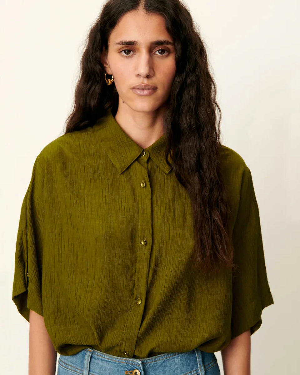 Luźna, krótka koszula Kayla Agave Green marki Sessun z klasycznym kołnierzykiem i krótkim rękawem z biżuteryjnymi guzikami przy mankietach. Zapinana z przodu na ozdobne guziki. Na plecach posiada płaskie zakładki, które dodają lekkości. Wykonana z mieszanki z wiskozą. To idealna propozycja na cieplejsze dni.&nbsp;

-Luźny, krótki fason

-Ozdobne guziki

-Zamów koszulę w swoim standardowym rozmiarze