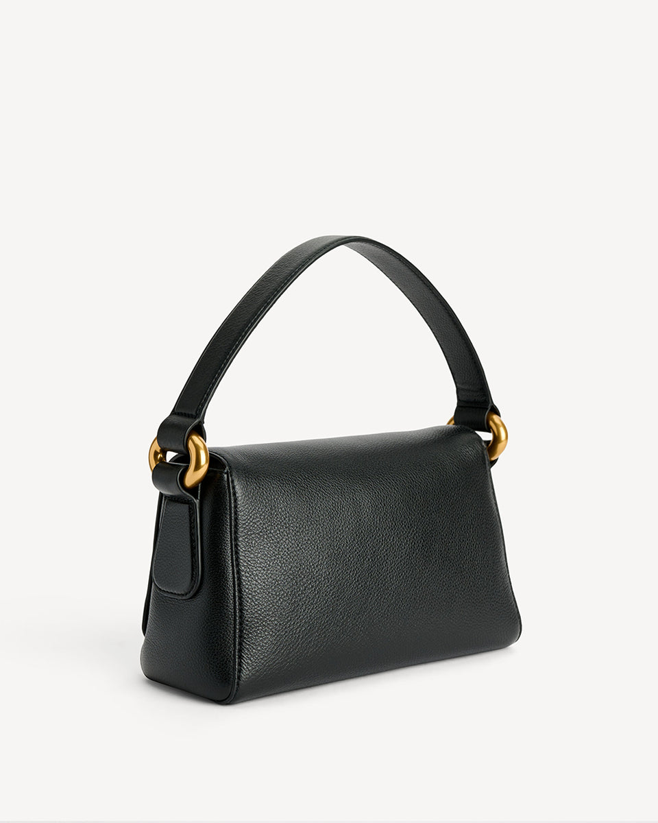 Minimalistyczna, elegancka torebka Lellie Black By Malene Birger o prostokątnym kształcie z lekko zaokrąglonymi bokami. Zapinana na zatrzask magnetyczny. Posiada krótki, szeroki pasek na ramię, który ozdobiony jest złotymi elementami. Na środku klapy umieszczono metalowy emblemat marki w kolorze złotym. W środku znajduje się mała kieszonka na drobiazgi, a całość wykończona jest gładką podszewką. Wykonana w 100% ze skóry.&nbsp;
