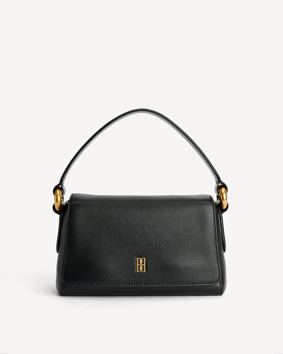 Minimalistyczna, elegancka torebka Lellie Black By Malene Birger o prostokątnym kształcie z lekko zaokrąglonymi bokami. Zapinana na zatrzask magnetyczny. Posiada krótki, szeroki pasek na ramię, który ozdobiony jest złotymi elementami. Na środku klapy umieszczono metalowy emblemat marki w kolorze złotym. W środku znajduje się mała kieszonka na drobiazgi, a całość wykończona jest gładką podszewką. Wykonana w 100% ze skóry.&nbsp;