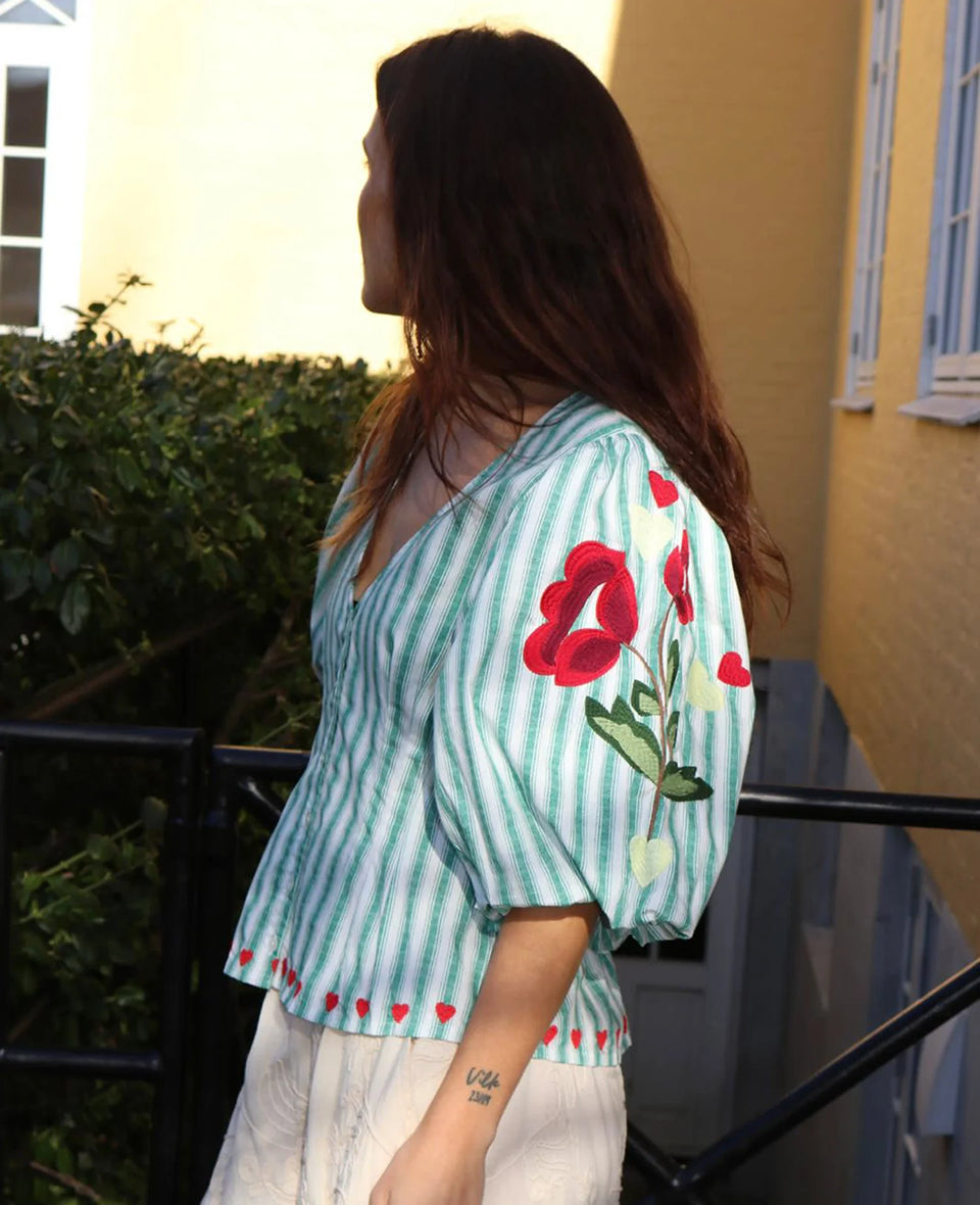 Kobieca bluzka koszulowa Lotta Green Stripes SISSEL EDELBO z dopasowaną talią i marszczeniem z tyłu. Ma głęboki dekolt w serek i zapięcie z przodu na guziki z masy perłowej. Rękawy mają długość 3/4 i zakończone są gumką. Ozdobiona jest delikatnym haftem kwiatowym i serduszkami. Wykonana z organicznej bawełny popelinowej w paski.&nbsp;

-Dopasowana talia

-100% bawełna organiczna

-Zamów bluzkę w swoim standardowym rozmiarze&nbsp;
