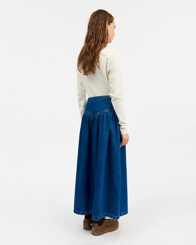 Romantyczna, długa, jeansowa spódnica Dolly SKALL z wysokim stanem. Odcięta nisko w talii, marszczona i rozkloszowana. W pasie zapinana na trzy guziki. Spódnica ma długość do kostek.