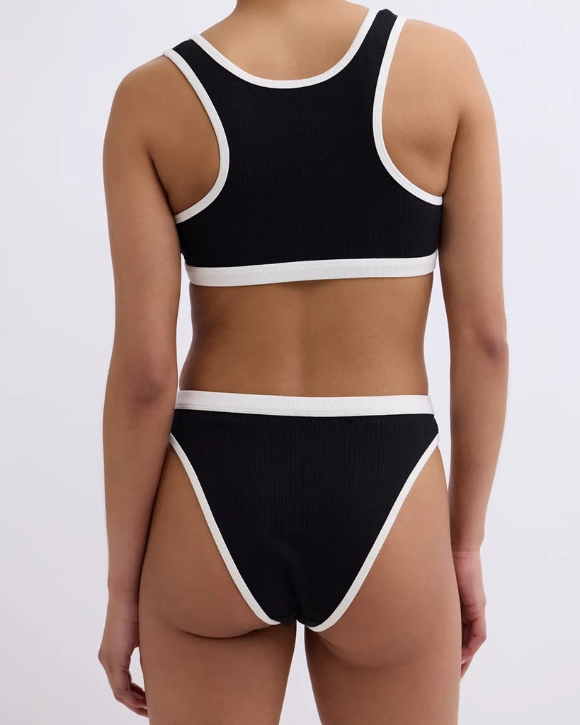 Miękki sportowy stanik top Rika Love Love Stories na grubych ramiączkach. Wykonany z miękkiej tkaniny z prążkowaną fakturą i białą, grubą lamówką. Na gumie pod biustem posiada niewielką naszywkę z logo marki.&nbsp;