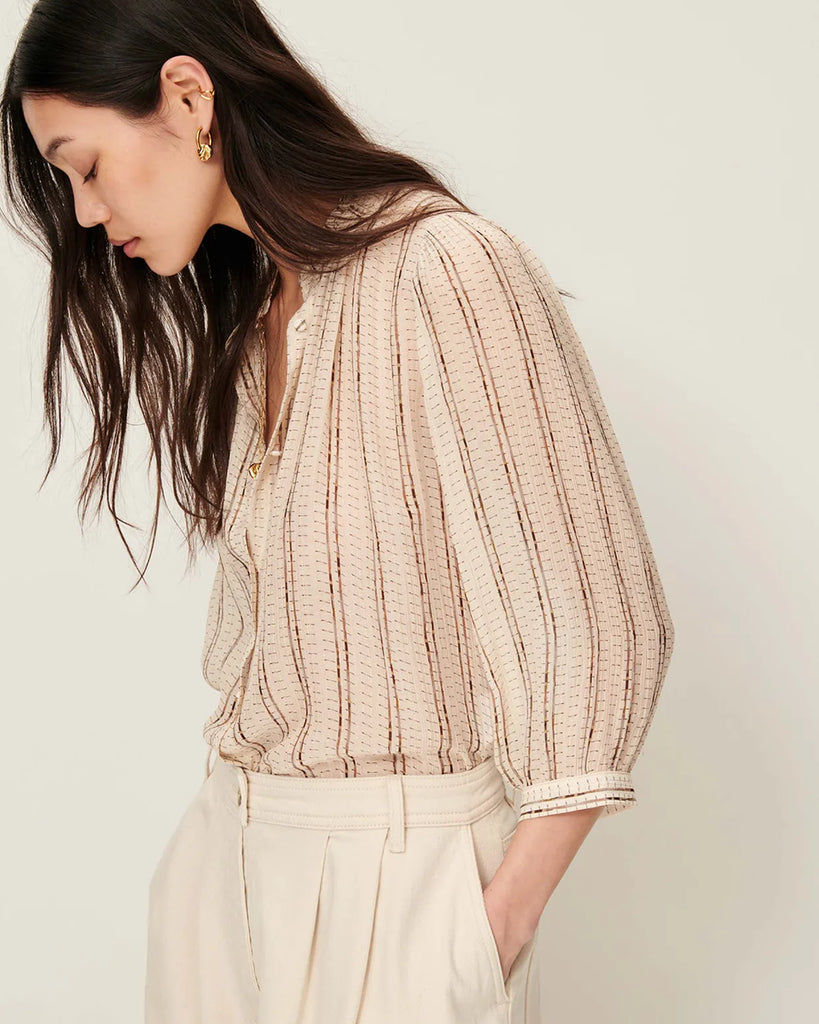 Efektowna, romantyczna Bluzka Lylee Whiplumikat francuskiej marki Sessun w drobne, metaliczne paski, z falbaniastym kołnierzykiem i szerokimi rękawami 3/4. Zapinana na guziki, z ozdobnym guzikiem przy kołnierzyku. Posiada marszczenia z przodu.