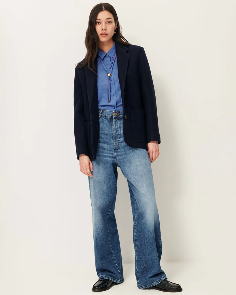 Granatowa, wełniana kurtka Madawool Navy w stylu garniturowym z lekko usztywnianymi ramionami. Ma dopasowany kołnierzyk, zapięcie na guziki z przodu i naszywane kieszenie. Posiada również ozdobne guziki przy mankietach.