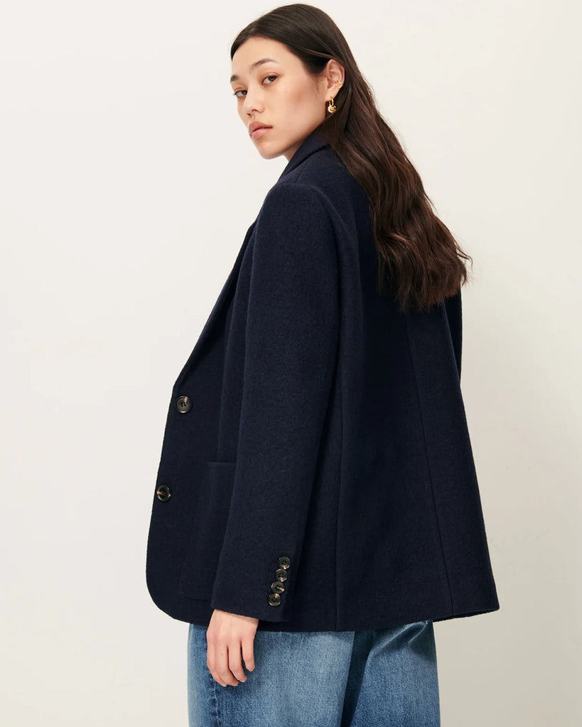 Granatowa, wełniana kurtka Madawool Navy w stylu garniturowym z lekko usztywnianymi ramionami. Ma dopasowany kołnierzyk, zapięcie na guziki z przodu i naszywane kieszenie. Posiada również ozdobne guziki przy mankietach.