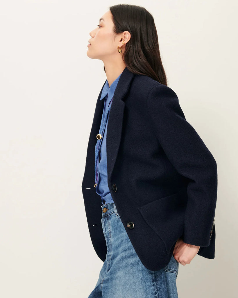 Granatowa, wełniana kurtka Madawool Navy w stylu garniturowym z lekko usztywnianymi ramionami. Ma dopasowany kołnierzyk, zapięcie na guziki z przodu i naszywane kieszenie. Posiada również ozdobne guziki przy mankietach.